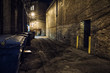 Dark and scary downtown urban city street corner alley with an eerie vintage industrial warehouse factory entrance and dirty dumpsters at night