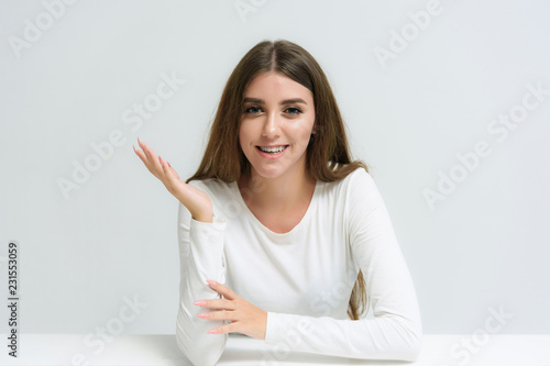 Fotografia Studio portrait of a smiling happy beautiful brunette girl on a white background talking and sitting at the table