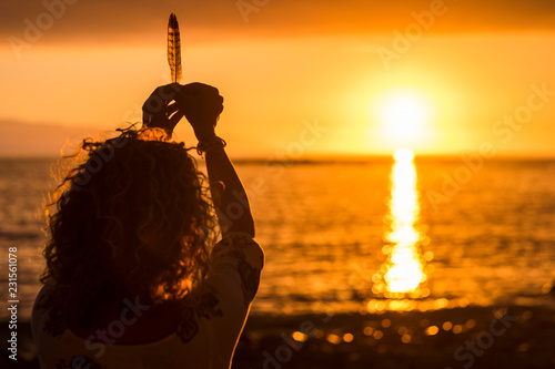 Freedom and meditation concept image with woman taking a  feather like life during a beautiful coloured orange and gold sunset on the sea. Nice tourism and vacation place with warm colors and love