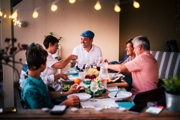 Dinner time in friendship with different ages people all together having fun and enjoying the night with smiles and happiness. Mobile phones defocused in for technology modern concept