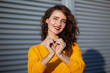 © vpavlyuk - Lifestyle shot: expressive brunette girl in yellow knitted sweater holding heart shaped hands, posing near shutters