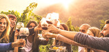 Young friends having fun outdoors - Happy people enjoying harvest time together at farmhouse winery countryside - Youth and friendship concept - Hands toasting red wine glass at vineyard before sunset