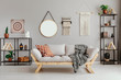Macrame, mirror and ethno graphic on beige wall in stylish living room interior with metal furniture and comfortable couch and patterned pillow and blanket