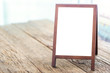 Mock up blank advertising whiteboard with easel standing on wood table in cafe and bar restaurant for display or montage of design space for text
