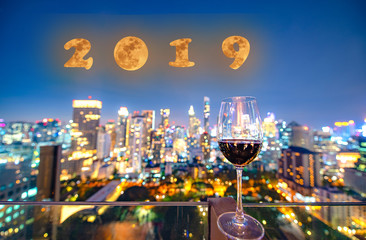 invitation on incoming year 2019 by glass of wine standing for celebration at night with the light bokeh of city shining in background, moon creat in concept celebration of 2019 in background