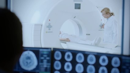 Wall Mural - In Medical Laboratory Patient Undergoes MRI or CT Scan Process under Supervision of Radiologist, in Control Room Doctor Watches Procedure and Monitors with Brain Scans Results.