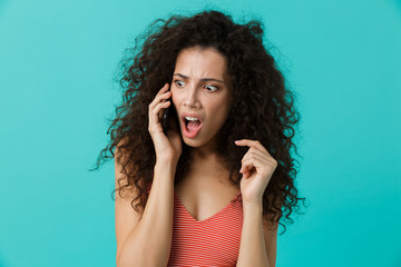 Wall Mural - Image of brunette woman 20s wearing casual clothing speaking on black mobile phone, standing isolated over blue background