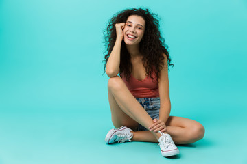 Canvas Print - Image of seductive woman 20s wearing casual clothing laughing while sitting on floor with legs crossed, isolated over blue background