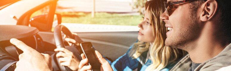 smiling man with smartphone showing direction to girlfriend that driving car