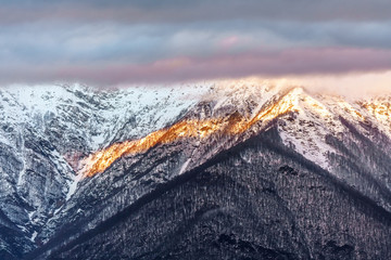 Wall Mural - Beautiful scenic winter sunset mountain landscape of Main Caucasus ridge with snowy mountain peaks covered with clouds, Sochi, Russia