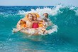 © Tropical studio - Happy kids have fun in sea surf on beach. Joyful couple of children on inflatable ring ride on breaking wave. Travel lifestyle, swimming activities in family summer camp. Vacations on tropical island