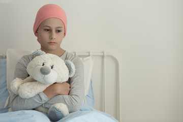 Sad girl with leukemia hugging plush toy in the hospital with copy space