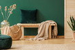 © Photographee.eu - Emerald green pillow and beige blanket on wooden bench in stylish interior designed with natural materials, real photo with copy space on empty green wall