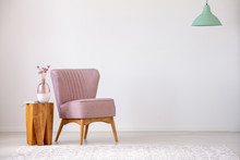 Flowers On Wooden Stool Next To Pink Armchair In Flat Interior With Copy Space And Mint Lamp. Real Photo