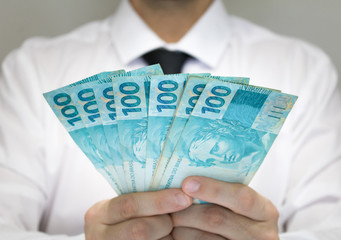 Close-up businessman wearing white shirt and black tie holding Brazilian money notes. Brazil one hundred (100) reais. Selective focus.