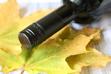 Bottle of wine and yellow maple leaves on wooden table. Autumn wine season