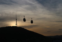 Two Aerial Tramway Cable Cars In Tbilisi Against The Sunset. In The Background The Television Tower Can Be Seen.
