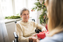 Health Visitor And Senior Woman In Wheelchair With A Present At Home At Christmas.