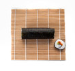 Rollo redondo de sushi con un maki sobre una esterilla visto cenitalmente y sobre un fondo blanco