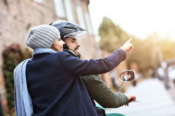 Beautiful young couple smiling while riding scooter in city in autumn