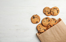 Paper Bag With Delicious Chocolate Chip Cookies On Wooden Table, Flat Lay. Space For Text