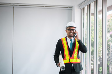 Asian man engineers using mobile phone and holding blueprint in office