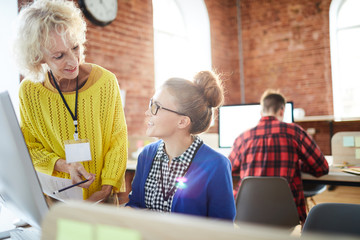 Canvas Print - Happy young and mature accountants discussing financial documents by workplace of one of them