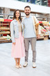 © pressmaster - Cheerful beautiful young couple in casual clothing standing in farmers market and smiling at camera, they buying food together