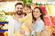 © pressmaster - Cheerful friendly young family embracing and standing organic food store while looking at camera