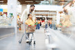 © pressmaster - Serious girl sitting in shopping cart and pointing with finger at shelf while helping father with shopping in supermarket