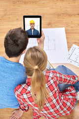 Canvas Print - repair, building and technology concept - close up of couple with blueprints having video call with builder or foreman on tablet pc computer at home