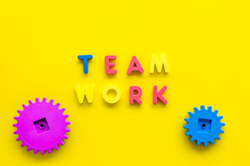 Teamwork concept. Text teamwork lined with colored letters near toy gears on yellow background top view space for text