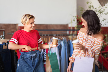 sale, shopping, fashion and people concept - happy young women with takeaway coffee cups choosing cl