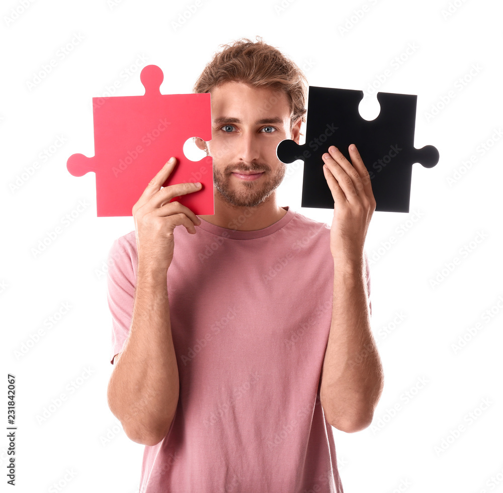 Young man with pieces of jigsaw puzzle on white background