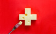 Swiss cross in form of cheese on red background, with a piece on fork