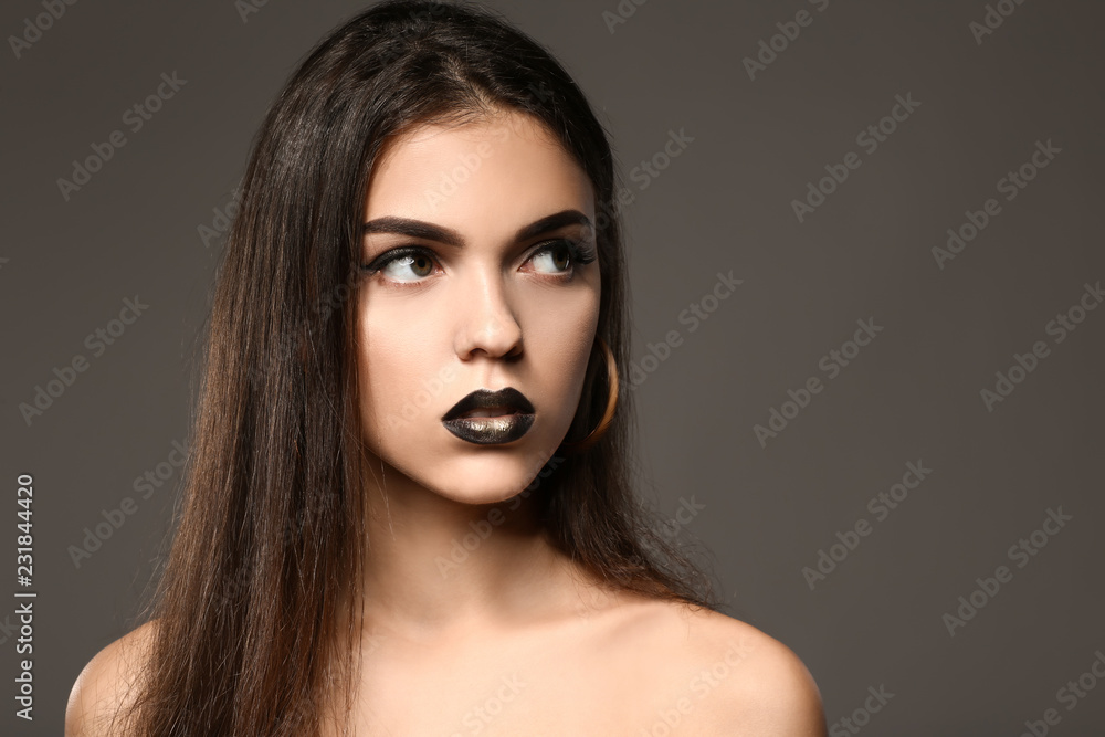 Beautiful young woman with extravagant makeup on grey background