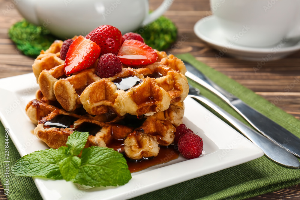 Tasty waffles with sweet syrup and berries on plate