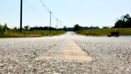 long stretch of empty highway with two solid yellow lines on the urban country road in the middle with grass and trees on either side on a cloudy summer day.