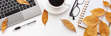 Panoramic Photo Of Wwhite Desk Seen From Above With A Laptop Keyboard, Notebook, Glasses, Coffee, Pen And Yellow Autumn Leaves