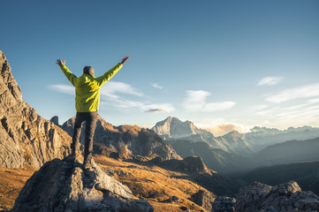 Wall Mural - sporty man standing on the stone with raised up arms against mountain valley at sunset. happy young 