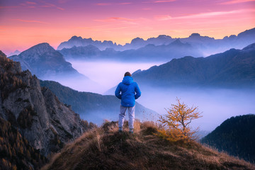 Wall Mural - sporty man on the mountain peak looking on mountain valley with low clouds at colorful sunset in aut