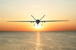 Unmanned military drone patrols the territory at sunset, flying above water surface. The view is straight ahead.