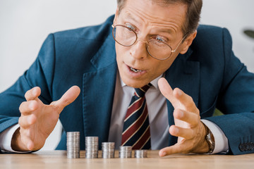 surprised businessman looking at silver coins at wooden table