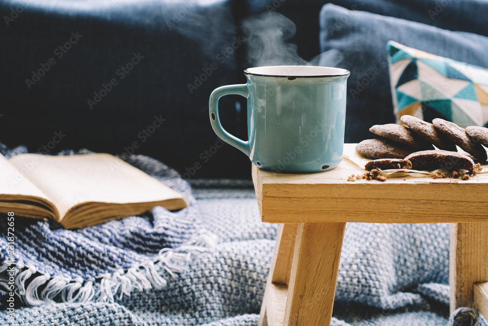 Cup of hot drink on wooden table. Living room interior with blue sofa on background. Cozy winter or autumn concept - obrazy, fototapety, plakaty 