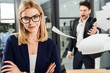 © LIGHTFIELD STUDIOS - selective focus of smiling businesswoman in eyeglasses and angry screaming boss throwing papers behind in office