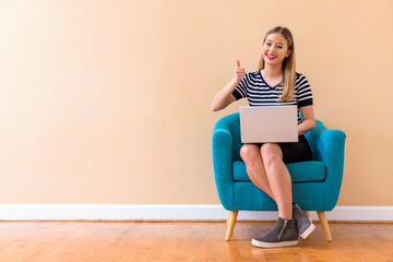 Wall Mural - Young woman with a laptop computer giving thumb up in a chair