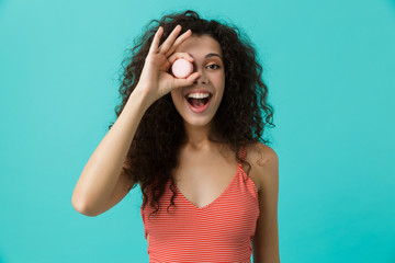 Poster - Photo of caucasian woman 20s with curly hair smiling and eating macaron biscuit, isolated over blue background