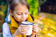 Child Girl Drinking Chocolate From A Cup Dressed In A Warm Yellow Vest In Autumn Scenery
