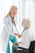 smiling female doctor examining with stethoscope disabled senior woman