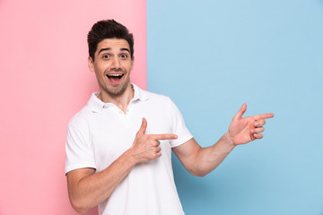 Canvas Print - Joyful man in casual t-shirt smiling and showing at copyspace on his palm, isolated over colorful background